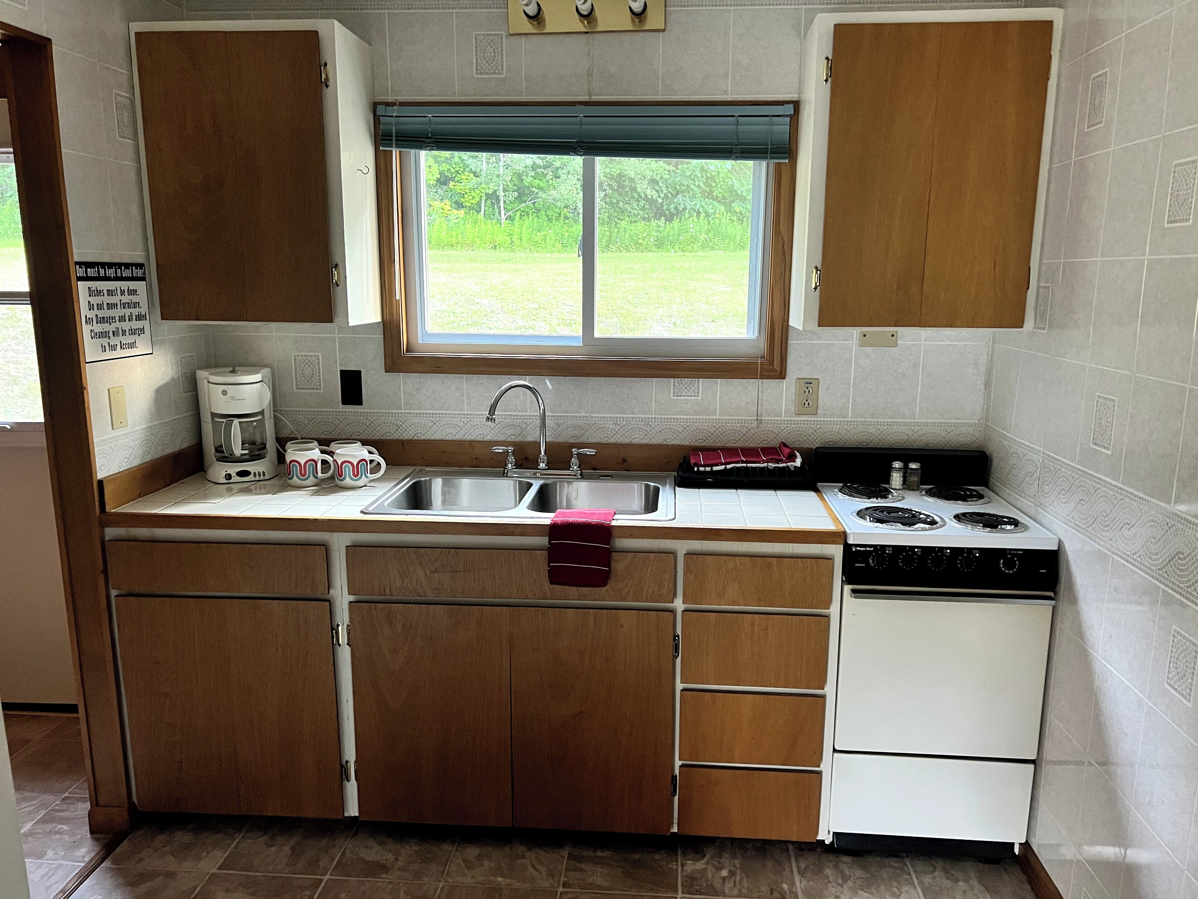Cocina con alacenas de madera, un lavamanos, estufa y ventana con vista a follaje.