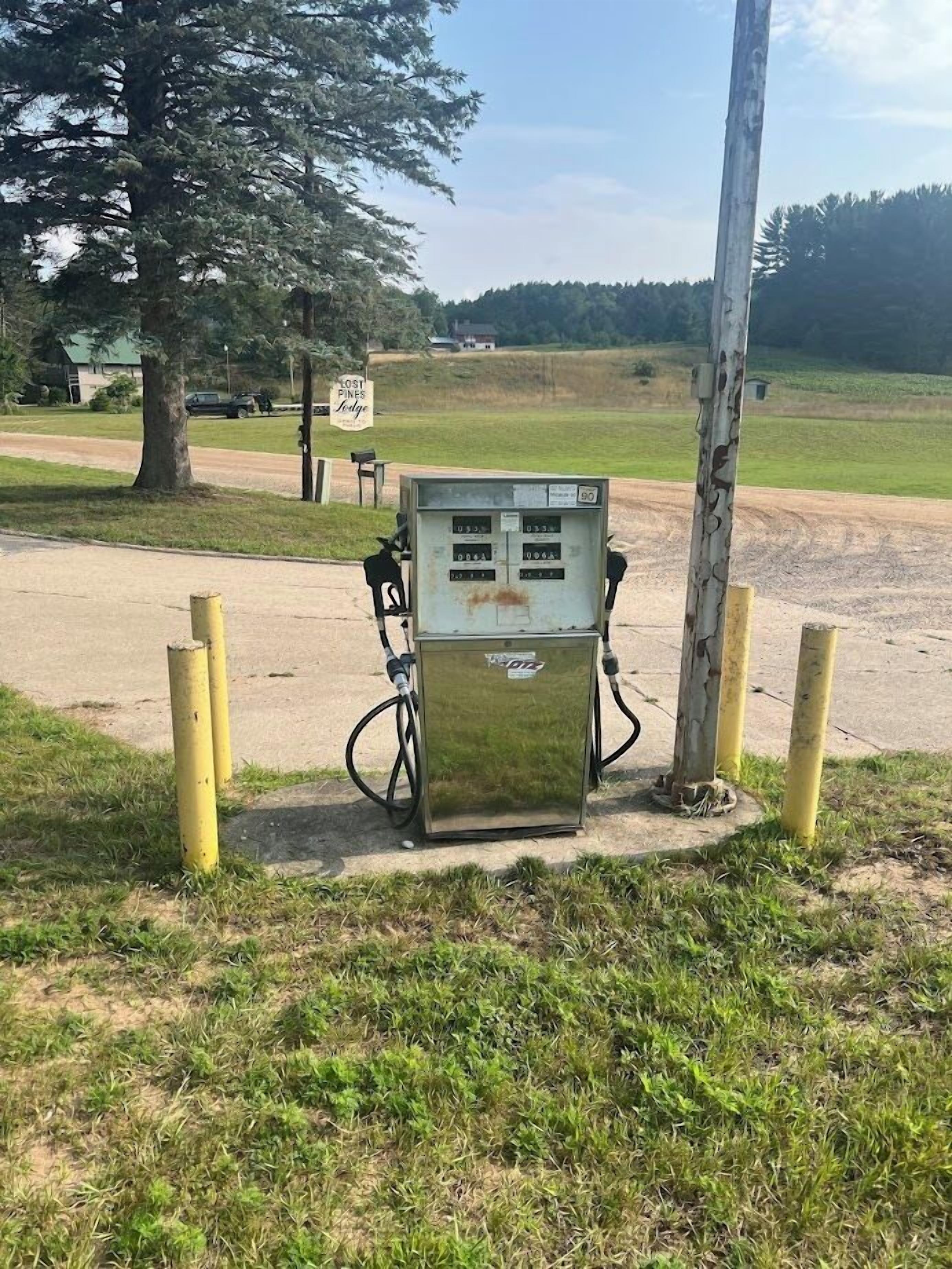 A utility box with multiple cables connected to it, situated in a grassy area with a dirt path and a tree in the background.