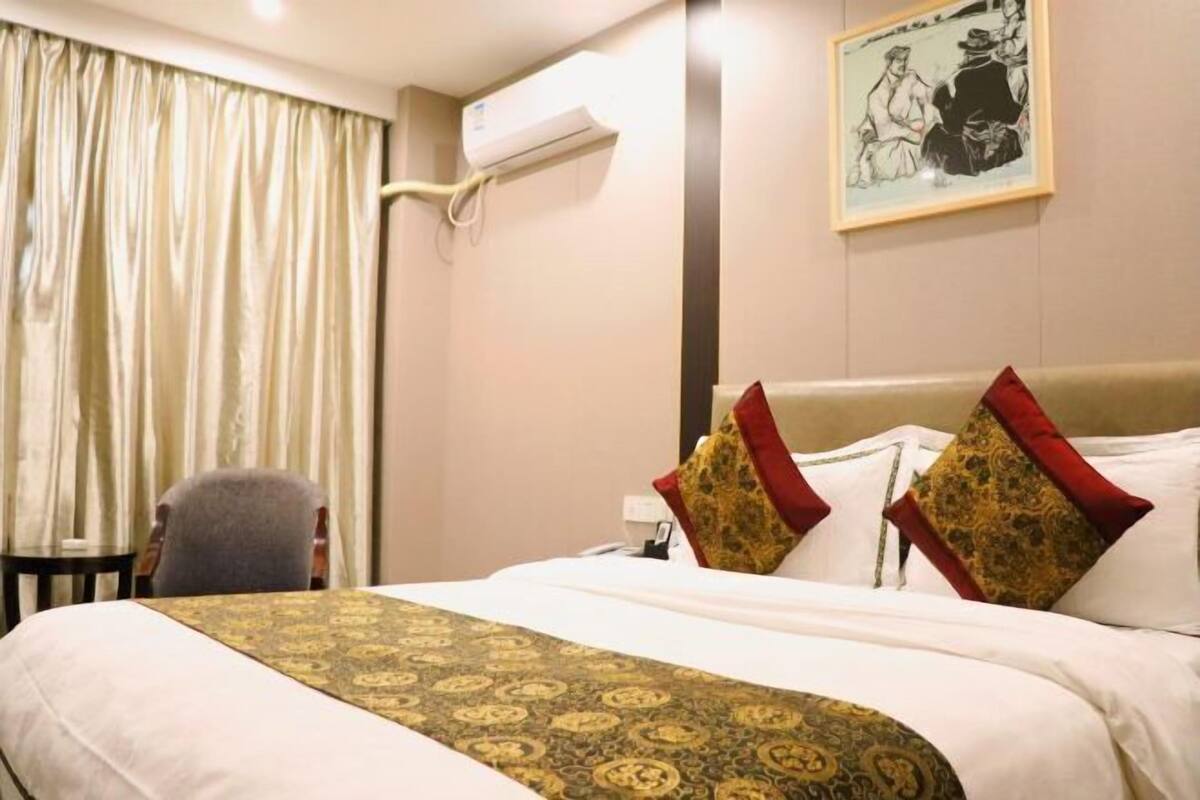 Habitación de hotel con cama, una silla, equipo de aire acondicionado y un cuadro en la pared.