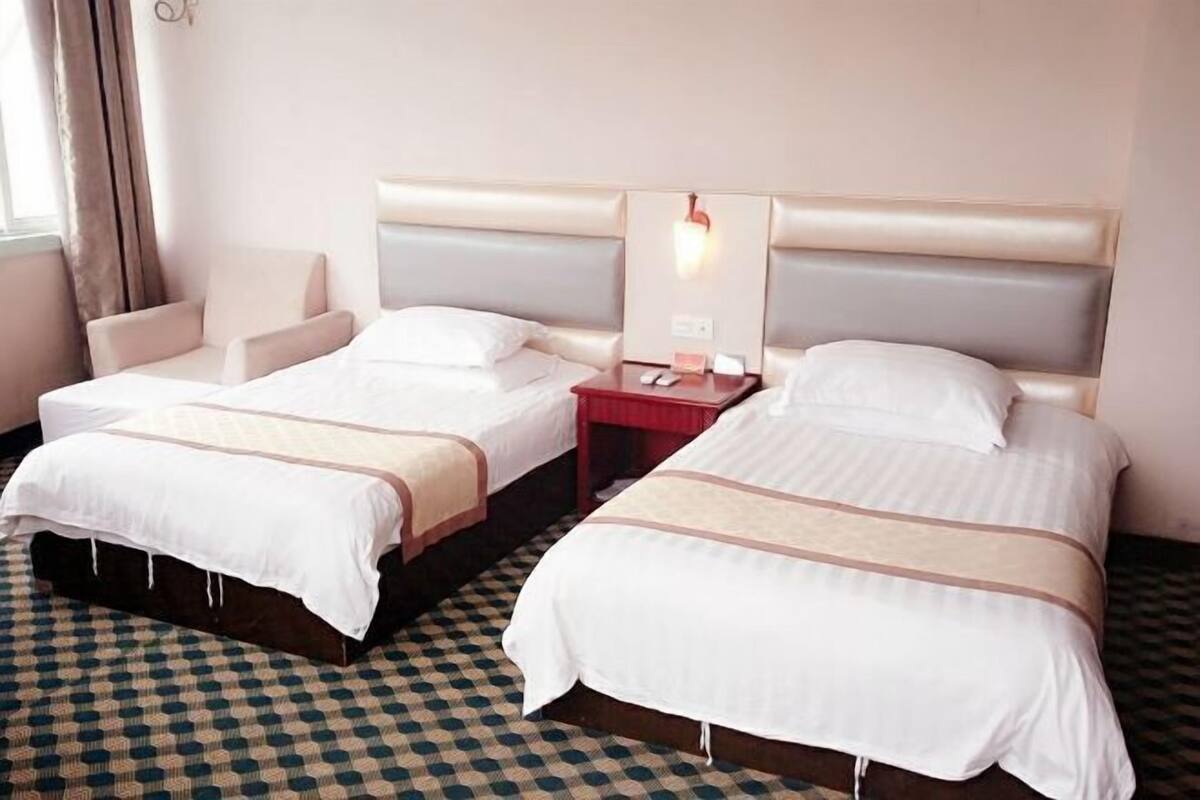 Una habitación de hotel con dos camas, una silla y una mesita de noche con lámpara.