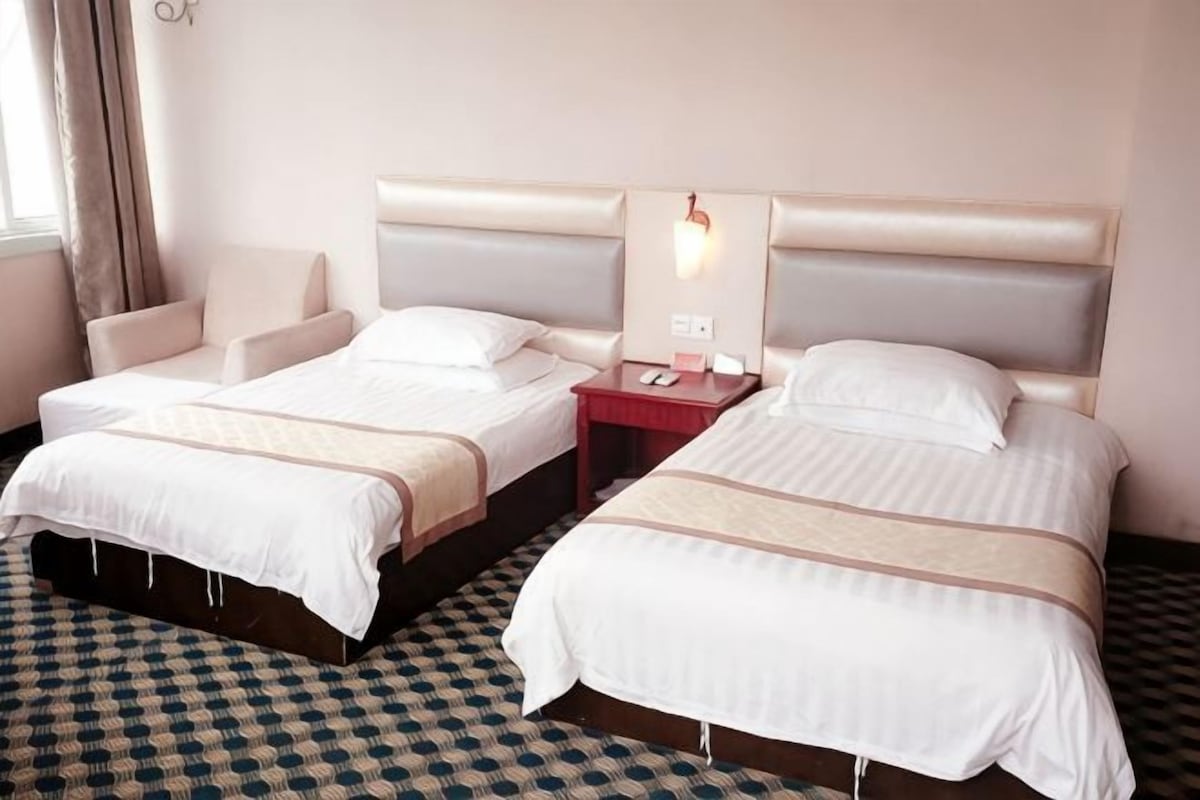 A hotel room with two beds, a nightstand, a lamp, and a check-in counter.