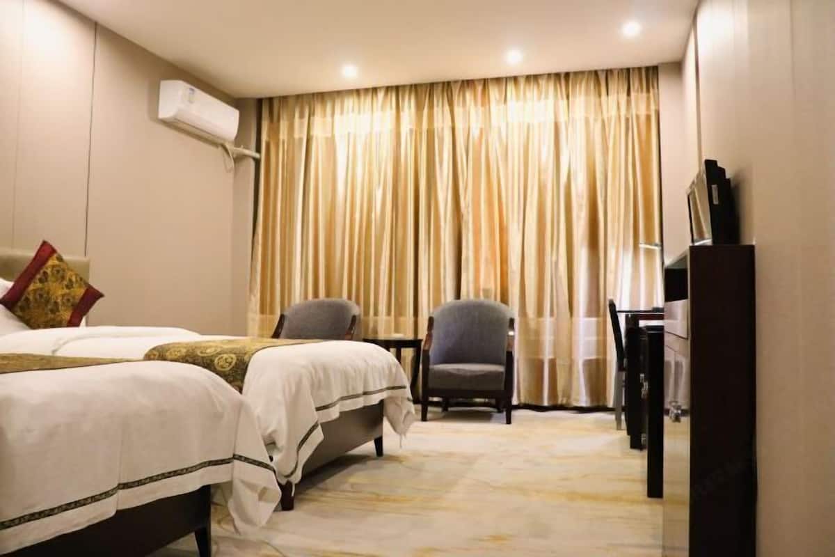 Habitación de hotel con cama, dos sillones, un escritorio y un gran ventanal con cortinas.
