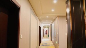 A hotel hallway with a carpeted floor, doors on both sides, and a light-colored ceiling with recessed lighting. - Baiyun Hotel (Shaoxing)