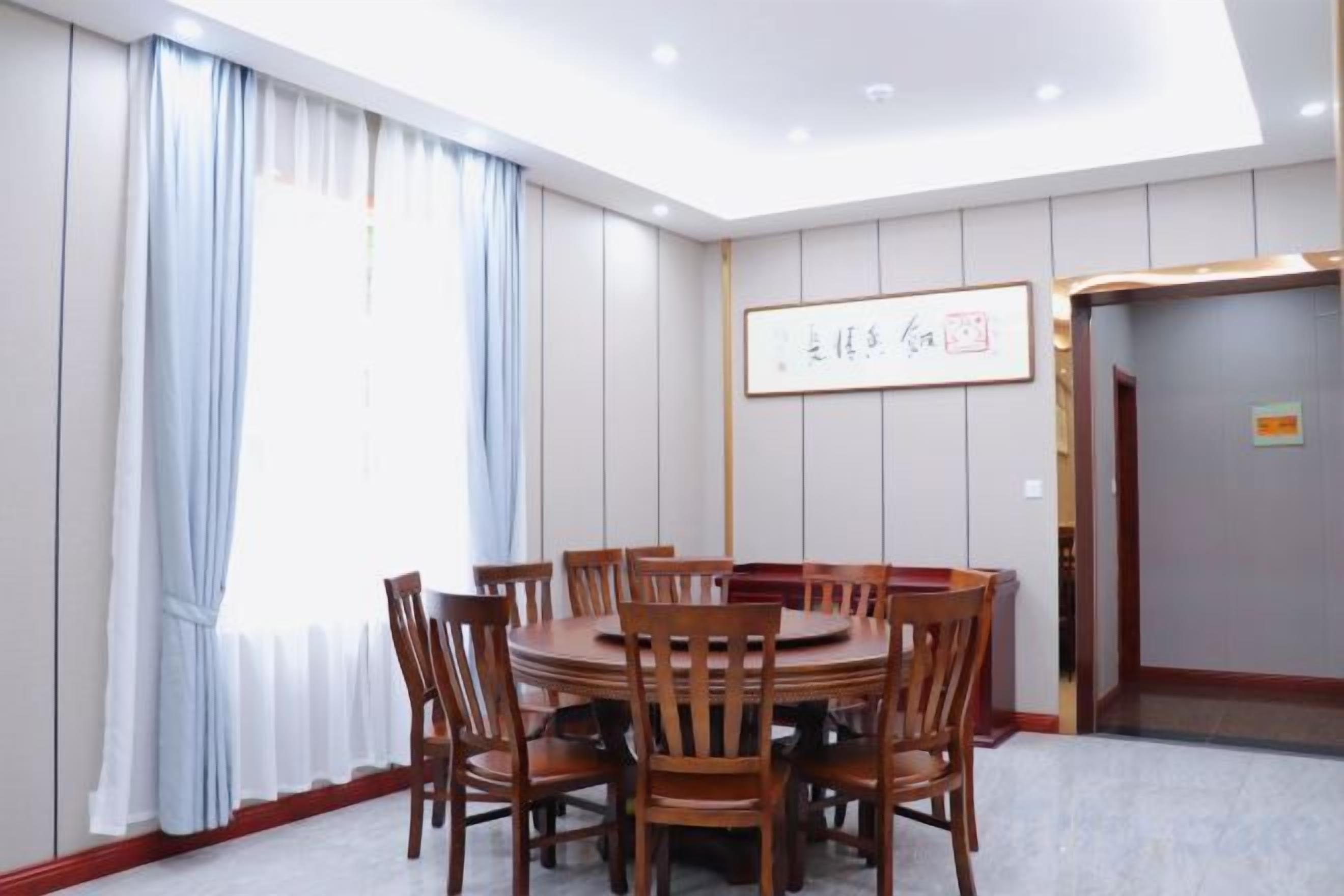 A conference room with a round table and chairs, a large window with curtains, and a framed sign on the wall.