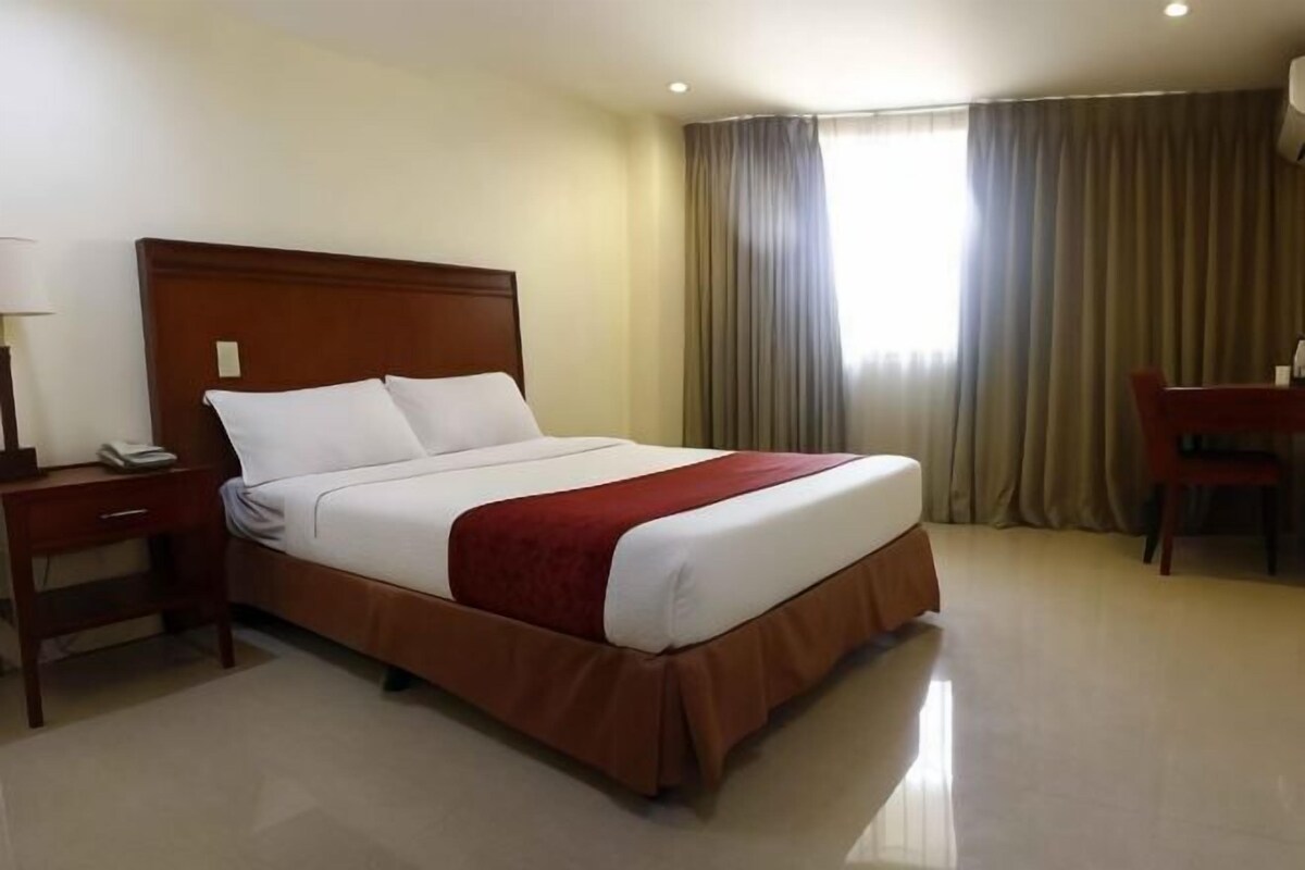 A hotel room with a bed, a desk, a chair, and a window with curtains.