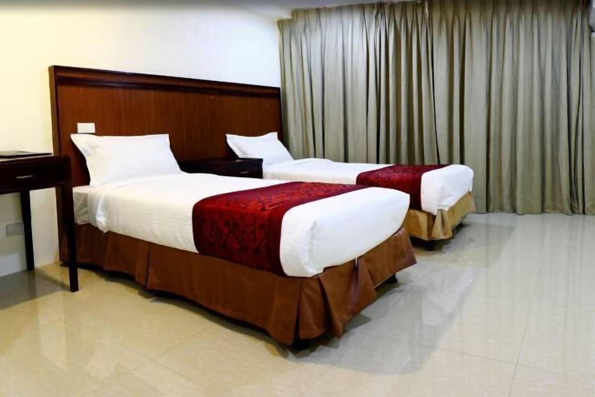 A hotel room with two beds, a wooden headboard, a nightstand, and a large window with curtains.
