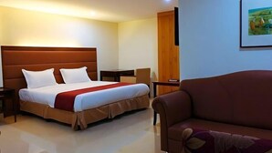 Een hotelkamer met een groot bed, een bank, een bureau en een schilderij aan de muur.