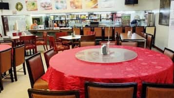 Ein Restaurant mit runden Tischen und Stühlen, eine Küche im Hintergrund und eine Speisekarte an der Wand.
