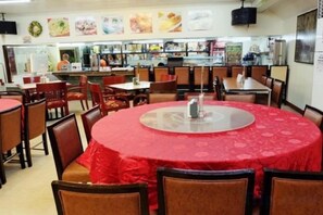 En restaurang med runda bord och stolar, ett kök i bakgrunden och en meny på väggen.