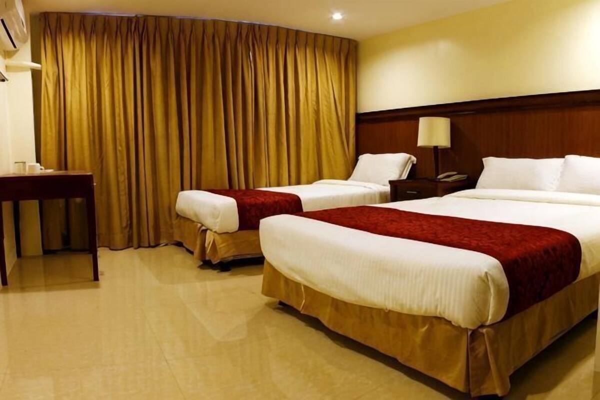 A hotel room with two beds, a desk, a nightstand, and a curtain.