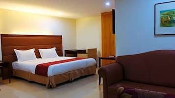 A hotel room with a bed, a sofa, a TV, and a painting on the wall.