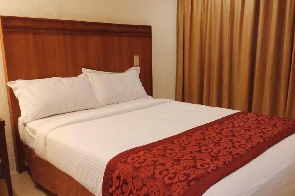 A hotel room with a wooden headboard, a white bedspread, and a red patterned throw blanket.