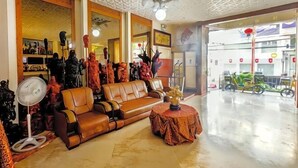 Een ruime woonkamer met een bruine leren bank, een ronde tafel en een ventilator.