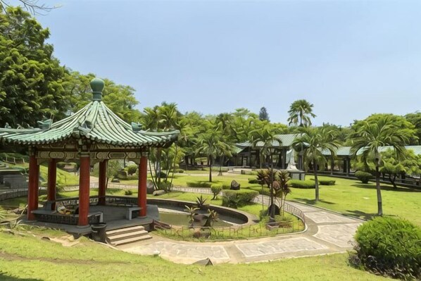 A traditional pavilion with a tiled roof, surrounded by a well-maintained garden with palm trees and a clear sky.