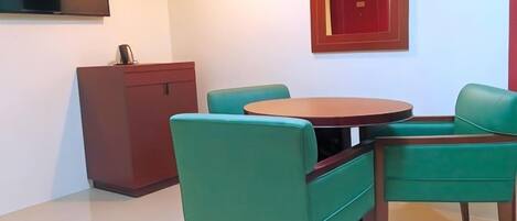 A room with a round table and four green chairs, a red cabinet, and a mirror on the wall.
