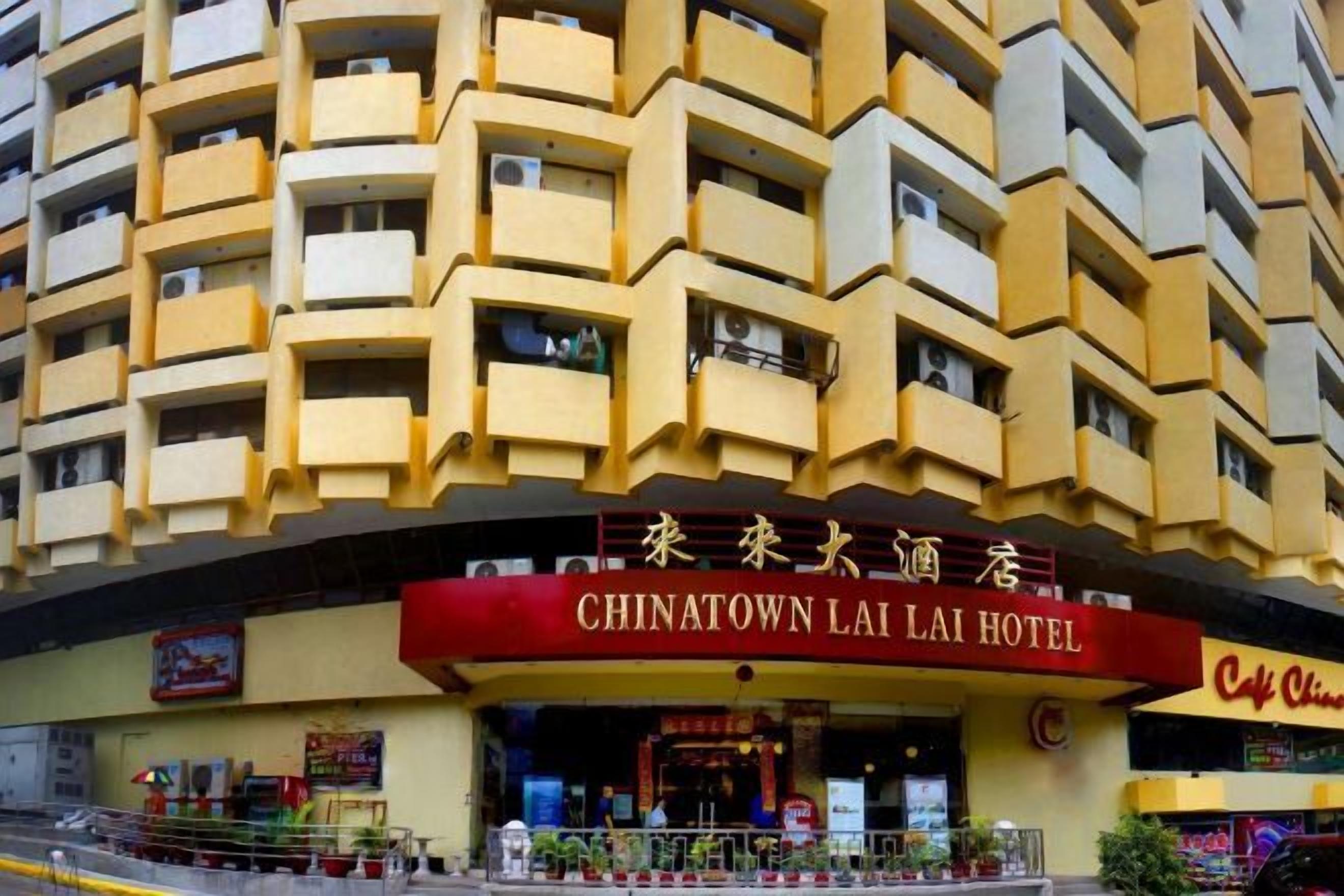 A hotel with a distinctive yellow facade, multiple balconies, and a prominent red sign indicating its name.