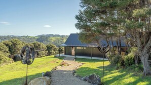 Una casa moderna con techo metálico, rodeada de un paisaje natural y un camino de grava que lleva a la entrada.