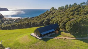 Una casa moderna con techo inclinado, ubicada en una colina cubierta de hierba con vistas a la costa y las islas distantes.