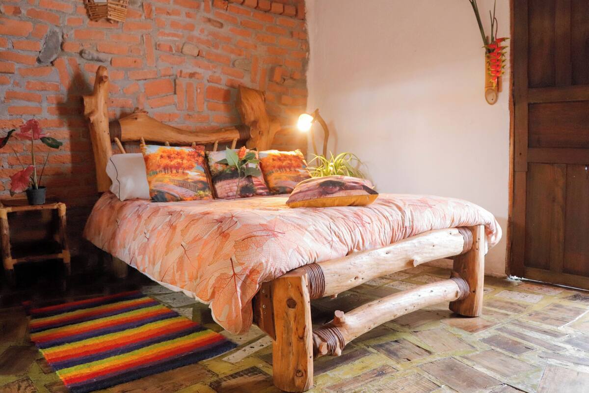 Un dormitorio rústico con pared de ladrillo, estructura de cama de madera y puerta de madera.