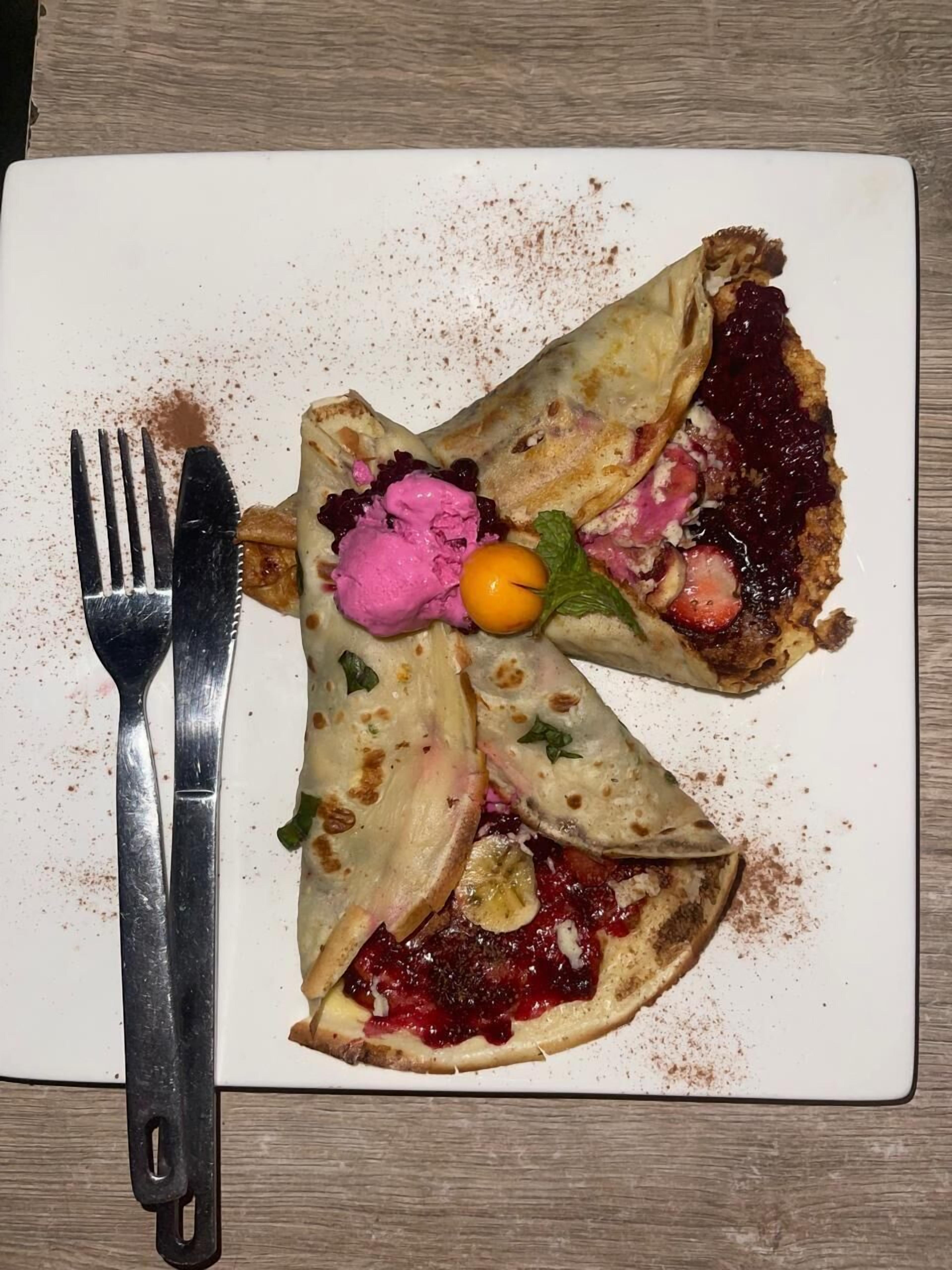 A plate with a crepe, berry compote, and a dollop of pink cream.