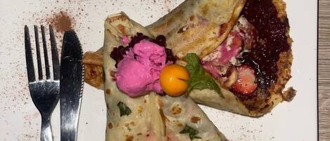 A plate with a crepe, berry compote, and a dollop of pink cream.