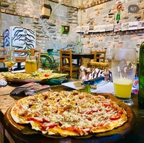 Un comedor rústico con una pizza grande, bebidas y una bicicleta al fondo.