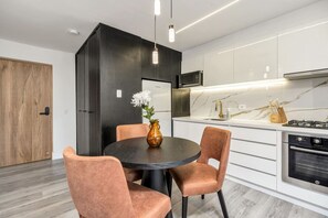 A modern kitchen with white cabinets, a black countertop, and stainless steel appliances. There is a round table with chairs and a vase with flowers. - delite* Elite Heaven:Luxurious1Bed+1bath (Medellín)