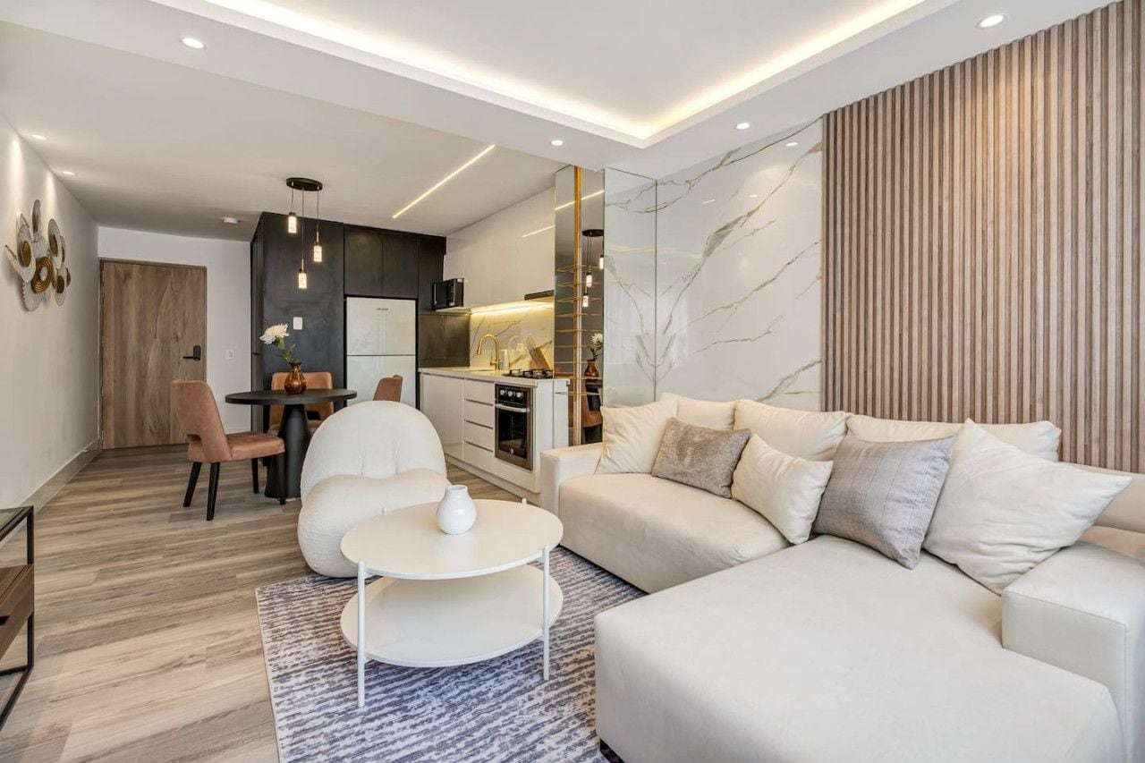 A modern living room with a sofa, a dining table, and a kitchen area.