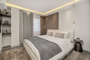 A modern bedroom with a large bed, bedside tables, a wall-mounted air conditioner, and a window with curtains.