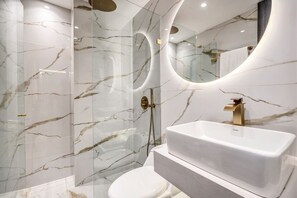 A modern bathroom with a marble wall, a white sink, and a glass-enclosed shower area.