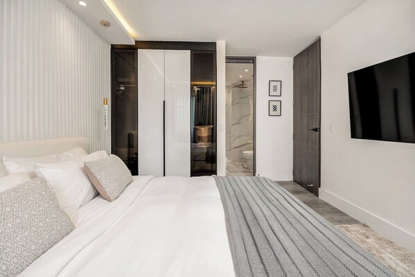 Une chambre moderne avec un grand lit, un téléviseur fixé au mur et un dressing.