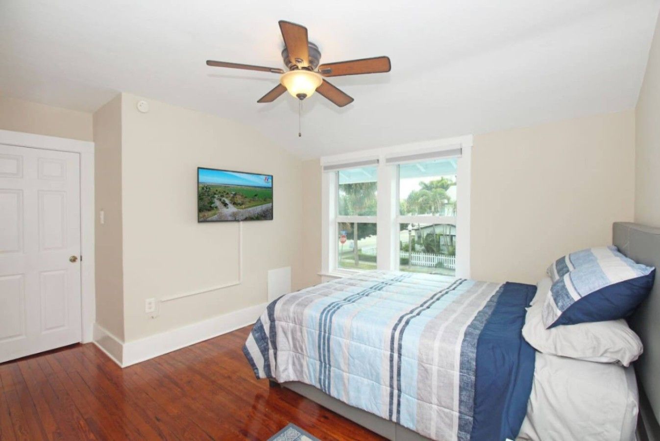 A bedroom with a bed, a ceiling fan, a window, and a door.