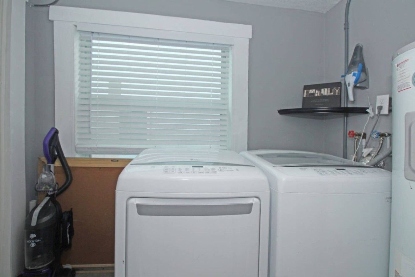 A laundry room with two front-loading washers and dryers, a vacuum cleaner, and a shelf with a hairdryer.