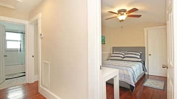 Een slaapkamer met een bed, een plafondventilator, een nachtkastje en een deur.