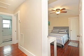 Un dormitorio con cama, ventilador de techo, mesita de noche y una puerta.