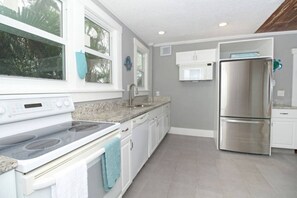 Una cocina con gabinetes blancos, un refrigerador de acero inoxidable, un horno doble y una encimera de granito.