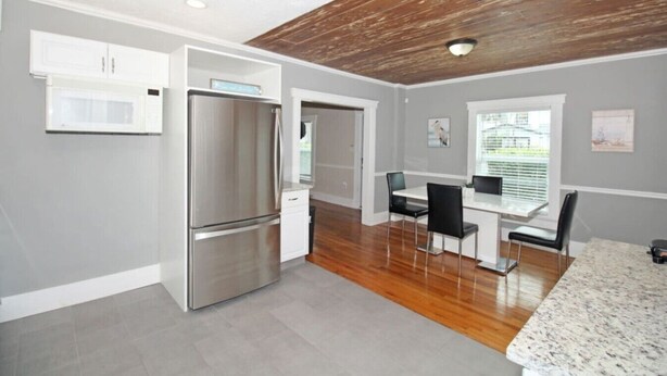 Una cocina moderna con refrigerador de acero inoxidable, armarios blancos y una zona de comedor con mesa y sillas.
