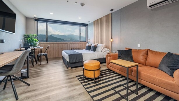 A modern, well-lit room with a bed, a sofa, a dining area, and a large window offering a mountain view. - ✨Perfect Studio✨View+COwork+NewBuilding+FastWIFI (Medellín)
