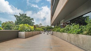 Ein modernes Gebäude mit einer gefliesten Promenade, Betonpflanzgefäßen mit Grünpflanzen und großen Fenstern.