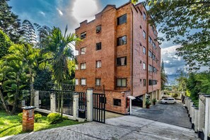 A multi-story brick building with a gated entrance, surrounded by greenery and a parked car. - High End Apartment 1 BD  1 BA Views Ac Malls (Medellín)