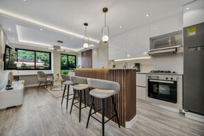 A modern kitchen with a central island, bar stools, and a view of greenery outside. - High End Apartment 1 BD  1 BA Views Ac Malls (Medellín)