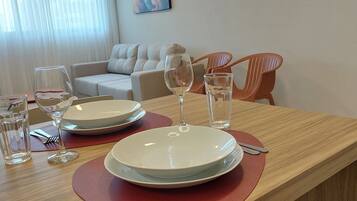 Et spisebord dækket med tallerkener, glas og bestik, med en sofa og stole i baggrunden.