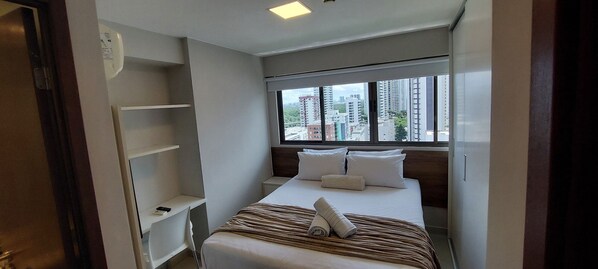 A hotel room with a bed, a window with a city view, a white wardrobe, and a small desk. - Flats at Beach Class Convention by Yolo (Recife)