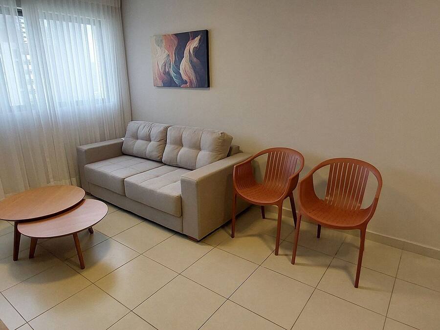 A living room with a sofa, two wooden tables, and two plastic chairs.