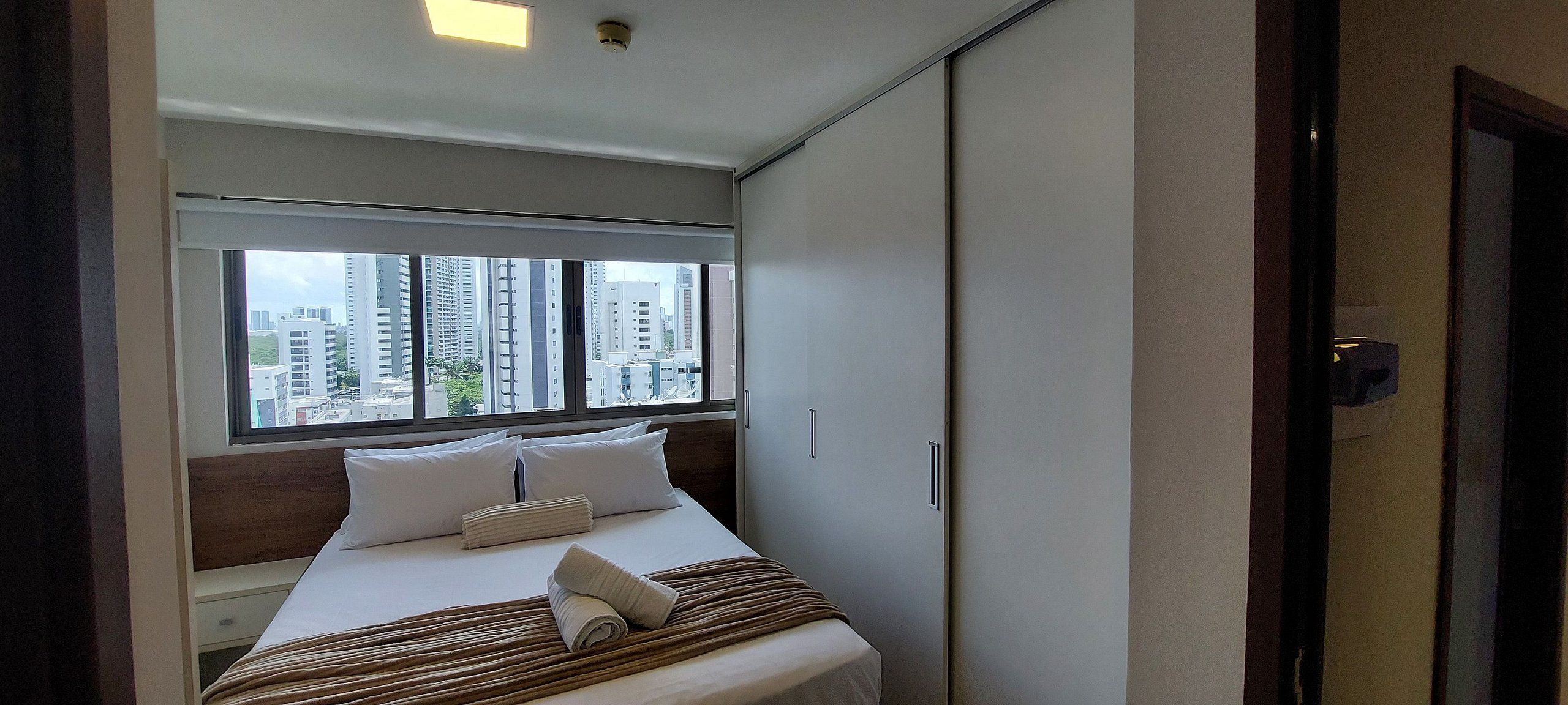 A hotel room with a bed, a window with a city view, and a wardrobe.