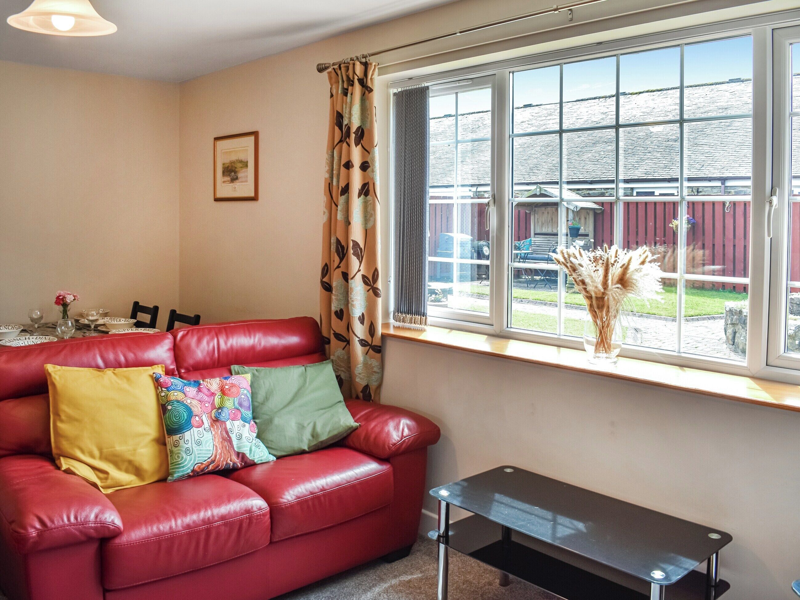 A red leather sofa with colorful cushions, a small black table, and a window with a view of a dock and water.