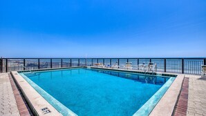 Ein rechteckiger Pool mit klarem, blauem Wasser, umgeben von einem schwarzen Metallzaun, mit Blick auf den Ozean im Hintergrund.