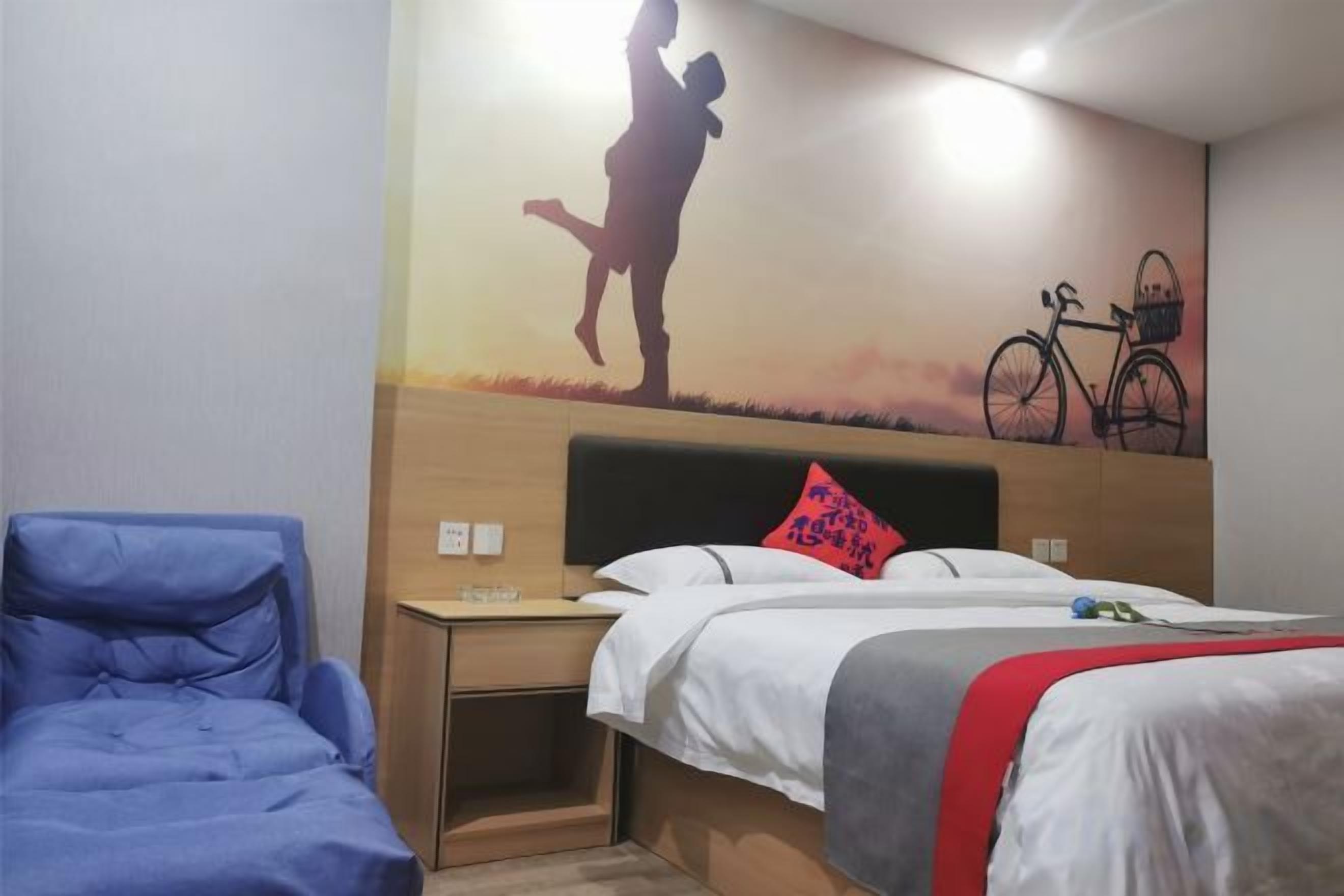 A hotel room with a bed, a nightstand, a blue chair, and a wall mural.