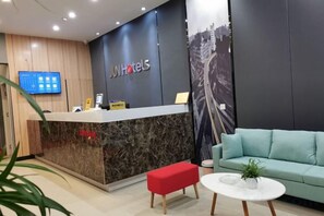 Een hotel receptie met een receptiebalie, een flatscreen televisie, een bank en een klein tafeltje met een plant.