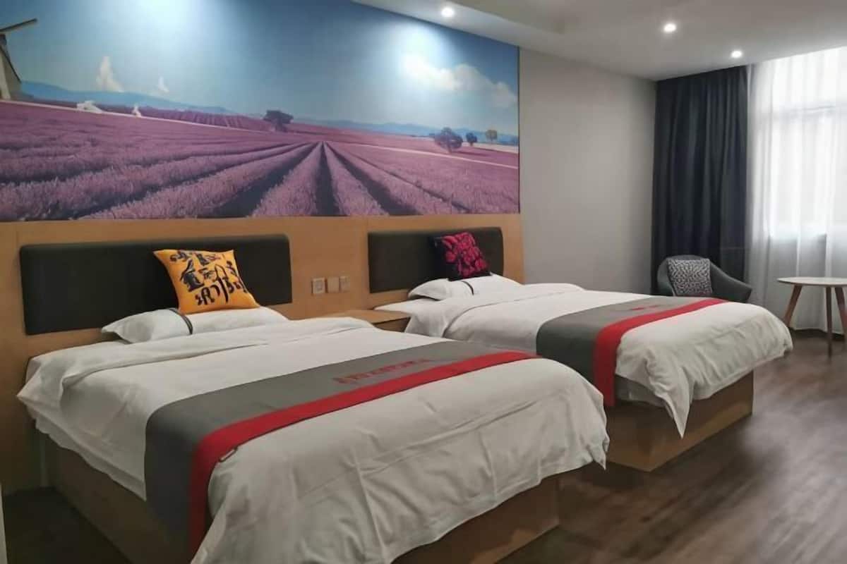 A hotel room with two beds, a mural of lavender fields, a small table, and a chair.